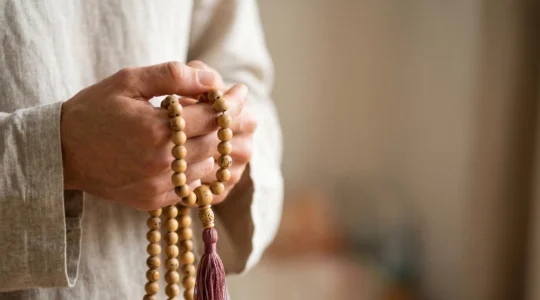 Mala de méditation en bois de santal tenu délicatement entre les doigts pour la récitation de mantras