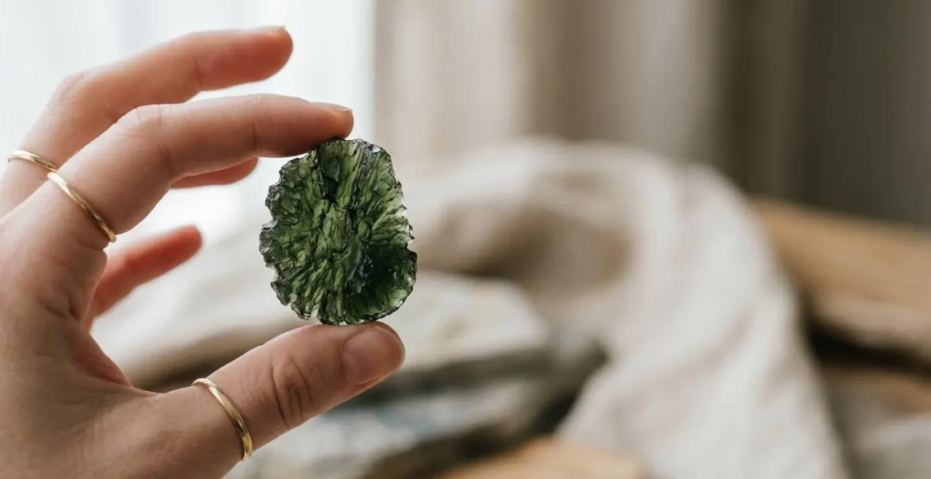 Pierre de moldavite verte tenue délicatement entre les doigts dans une lumière naturelle symbolisant la transformation et l'éveil spirituel