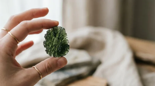 Pierre de moldavite verte tenue délicatement entre les doigts dans une lumière naturelle symbolisant la transformation et l'éveil spirituel
