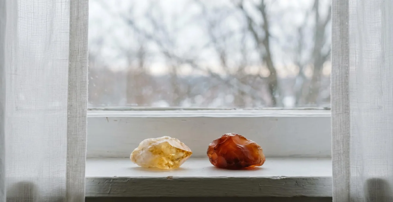Pierre de citrine jaune et cornaline orange disposées sur un rebord de fenêtre baigné de lumière douce hivernale